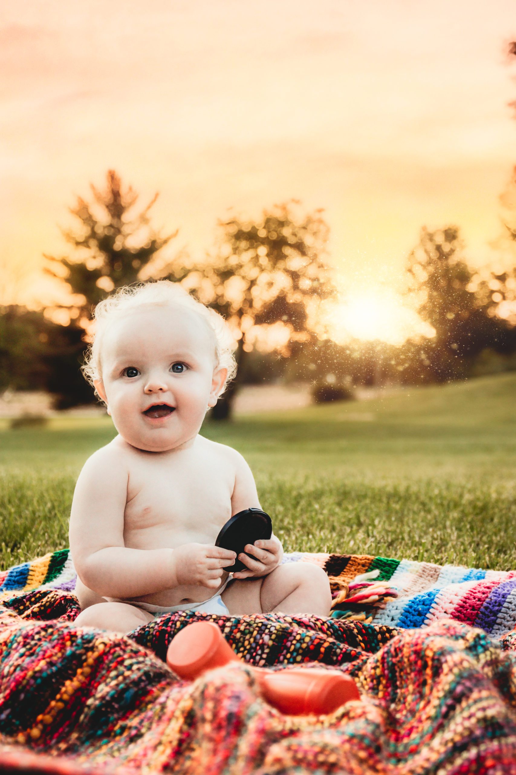 beautiful baby sitting on blanket with the golden sunset in the background.