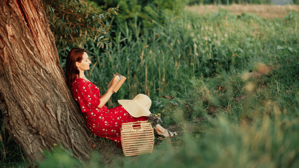 Embracing Imperfections: woman sits under a tree in a beautiful meadow journaling. 