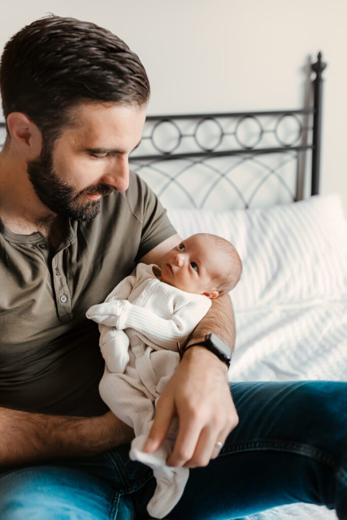 Capture the essence of parenthood with in-home newborn photography: A father's gentle touch as he holds his newborn close.