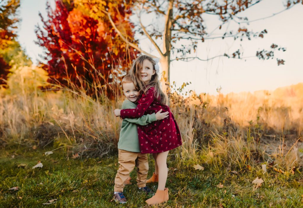 Siblings playing in a pile of colorful leaves, laughing and throwing leaves into the air.