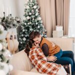 Family posing in a cozy studio setting, surrounded by holiday decorations, including twinkling lights and a beautifully decorated Christmas tree.