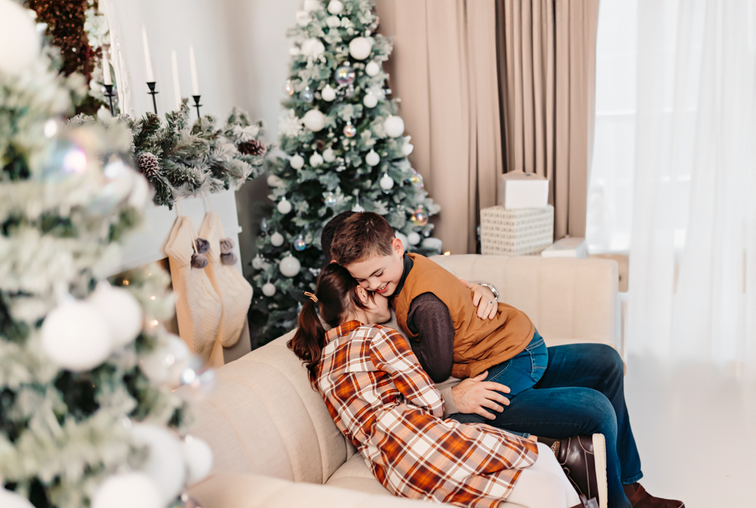 Family posing in a cozy studio setting, surrounded by holiday decorations, including twinkling lights and a beautifully decorated Christmas tree.